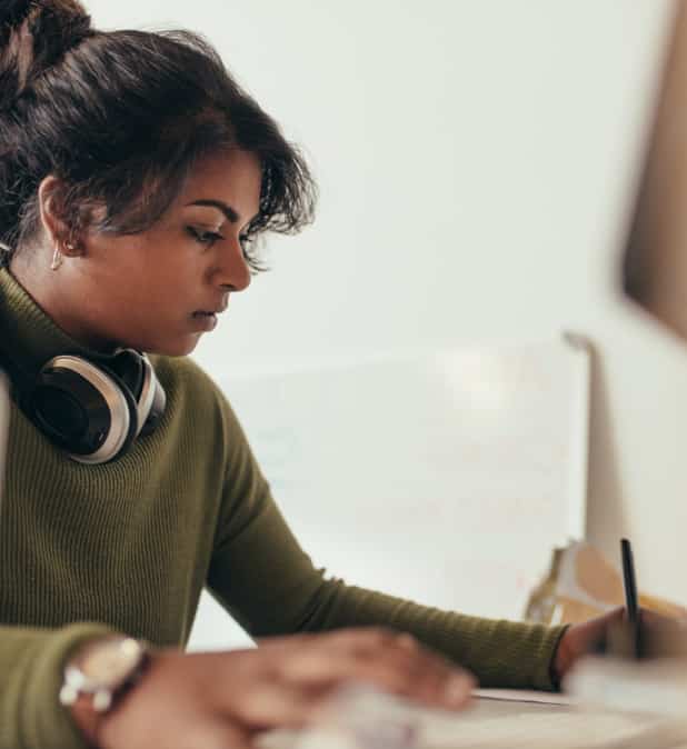 Woman taking notes in front of a computer monitor